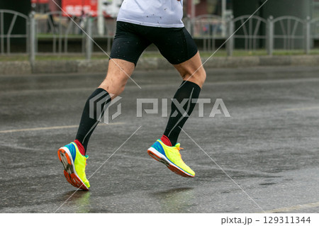 runner legs in compression socks and bright running shoes running on wet road runner legs in compression socks and bright running shoes running on wet road 129311344