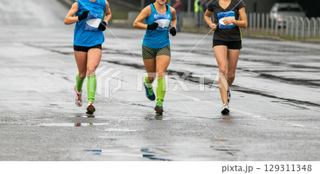 three young female athletes running marathon in cold weather on wet road three young female athletes running marathon in cold weather on wet road 129311348