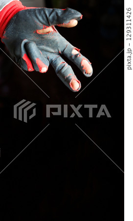 A powerful vertical shot capturing a damaged glove on a hand, with two fingers extended against a stark black background. This image is a poignant representation of poverty and hardship 129311426