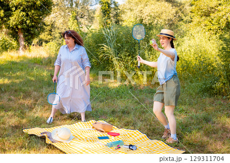 Caucasian family of two playing badminton with rackets in the park. Mother and daughter enjoying sport and quality time together. Caucasian family of two playing badminton with rackets in the park. Mother and daughter enjoying sport and quality time together. 129311704