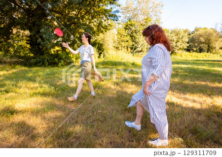 Caucasian woman and daughter throw frisbee in a natural green park area. Concept of vacation time, fitness, parenting and outdoor family entertainment. 129311709