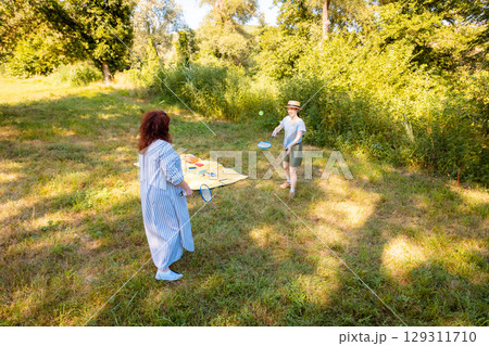 Caucasian woman and her daughter enjoy badminton in a green park with trees. Real people, outdoor game, bonding and holiday mood. Caucasian woman and her daughter enjoy badminton in a green park with trees. Real people, outdoor game, bonding and holiday mood. 129311710