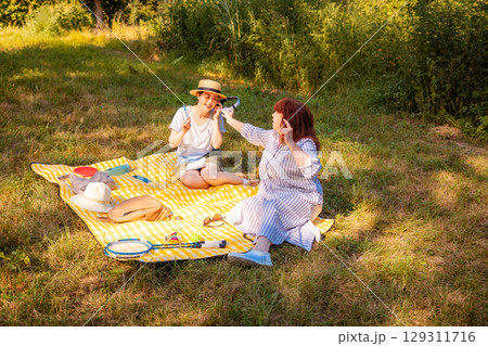 Happy family moment outdoors with mom and daughter talking and relaxing in green forest. Concept of female friendship and vacation. 129311716
