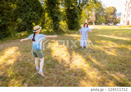 Middle aged mom and young daughter playing frisbee on sunny day in grassy park. Concept of fitness, recreation and parenting time. 129311722