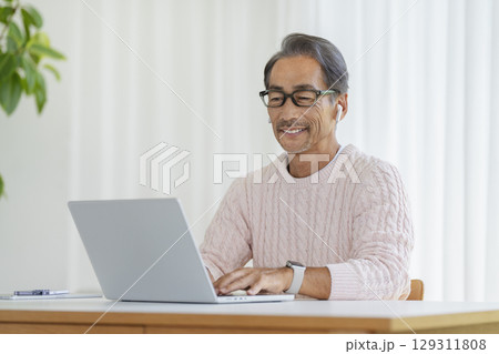 ノートパソコンで作業をするイヤホンをつけた60代の男性 ノートパソコンで作業をするイヤホンをつけた60代の男性 129311808