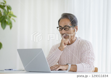 ノートパソコンに向かうイヤホンをつけた60代の男性 ノートパソコンに向かうイヤホンをつけた60代の男性 129311834