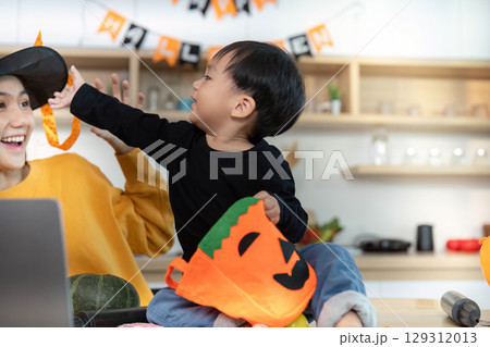 Halloween Fun. Child reaching for pumpkin basket while mother shares a smile. 129312013