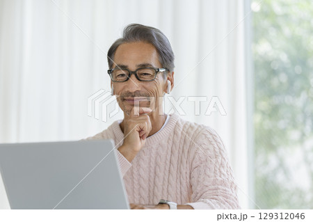 ノートパソコンの画面を見るイヤホンをつけた60代の男性 ノートパソコンの画面を見るイヤホンをつけた60代の男性 129312046