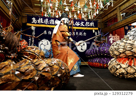 石見神楽 (夜神楽) 神社拝殿舞台で蜷局を巻く大蛇を退治しようとしている主人公の演者 石見神楽 (夜神楽) 神社拝殿舞台で蜷局を巻く大蛇を退治しようとしている主人公の演者 129312279