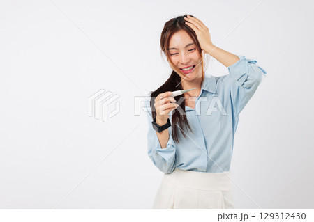 Smile Asian unwell woman with fever and headache is holding thermometer and touching head, feeling sick needing healthcare while checking her temperature using thermometer, isolated white background 129312430