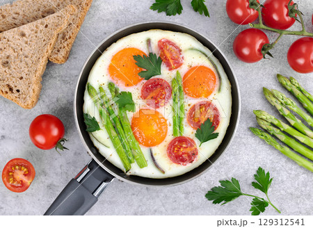 Fried eggs with vegetables asparagus, tomatoes and onions, toasts on a gray wooden background. Top view. Breakfast food. 129312541