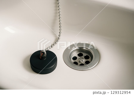 Sink drain with plug and metal chain in white ceramic basin 129312954