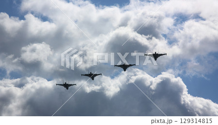 Formation of fighter jets soaring through a dramatic cloudy sky during a military display in early morning sunshine 129314815