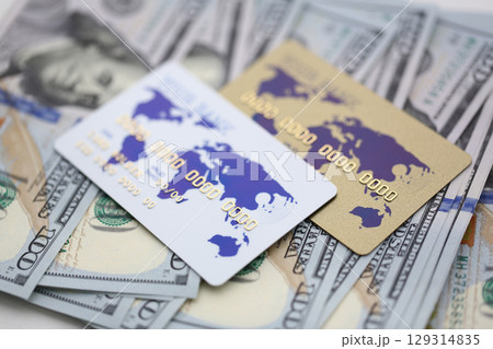 Colorful credit cards resting on a stack of hundred-dollar bills during a sunny afternoon in a bustling city market 129314835