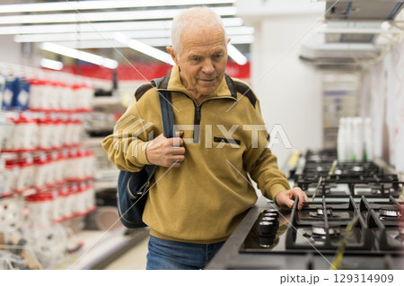 elderly grayhaired man pensioner looking gas hob at counter in showroom of electrical appliance hypermarket department 129314909