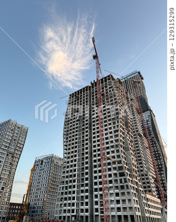 Construction site of modern high rise buildings with cranes and scaffolding. Concrete structures in development against a clear blue sky, showcasing the progress of an urban real estate project Construction site of modern high rise buildings with cranes and scaffolding. Concrete structures in development against a clear blue sky, showcasing the progress of an urban real estate project 129315299