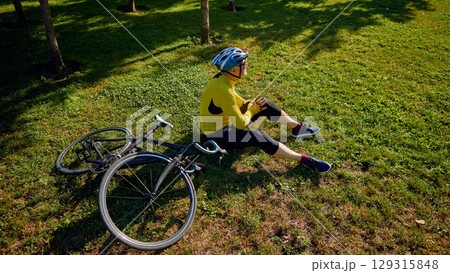 Cyclist resting on grass beside bicycle in shaded park area Cyclist resting on grass beside bicycle in shaded park area 129315848