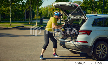 Senior man unloading road bike from car trunk in parking lot wearing cycling gear 129315869