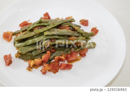 Fried green beans with tomato and onion pieces. Tasty meal with french bean on dinner or lunch on the white plate 129316983