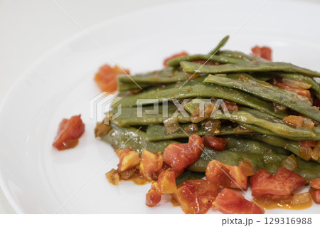Fried green beans with tomato and onion pieces. Tasty meal with french bean on dinner or lunch on the white plate Fried green beans with tomato and onion pieces. Tasty meal with french bean on dinner or lunch on the white plate 129316988
