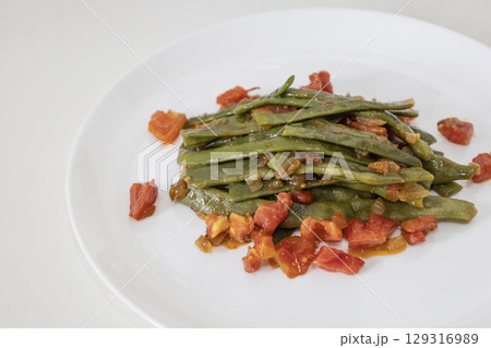 Fried green beans with tomato and onion pieces. Tasty meal with french bean on dinner or lunch on the white plate 129316989