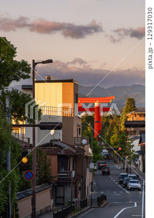 Red torii of Heian-jingu Shrine rising beyond rooftops in Kyoto during golden hour with calm traffic 129317030