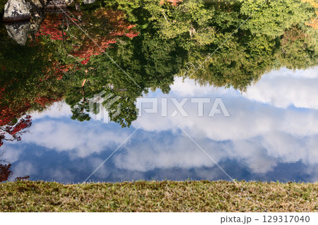 Mirror-like pond reflects red maple foliage, green trees, and drifting clouds blending earth and sky 129317040