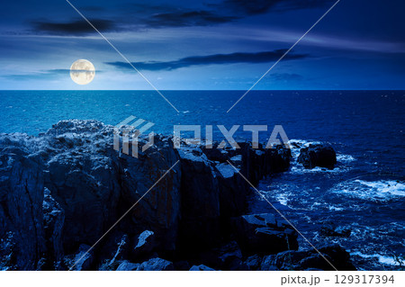 landscape with sea and coast with rock at night. vacation season with beautiful seascape in summer. travel background with water splash on stone in full moon light landscape with sea and coast with rock at night. vacation season with beautiful seascape in summer. travel background with water splash on stone in full moon light 129317394