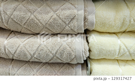 Close-up of several stacks of soft fluffy towels with diamond pattern in shades of beige and light yellow neatly folded and displayed on store shelf Close-up of several stacks of soft fluffy towels with diamond pattern in shades of beige and light yellow neatly folded and displayed on store shelf 129317427