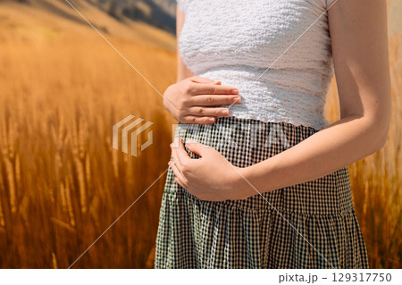 Pregnant Woman in Wheat Field. Close-up of a pregnant woman gently holding her belly while standing in a golden wheat field. Pregnant Woman in Wheat Field. Close-up of a pregnant woman gently holding her belly while standing in a golden wheat field. 129317750