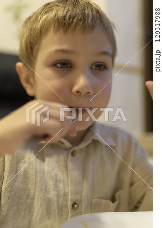 Blond boy eating with fork and looking away from camera 129317988