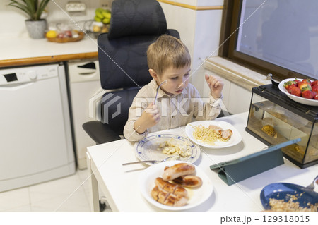 Blond child having lunch while watching tablet in kitchen 129318015