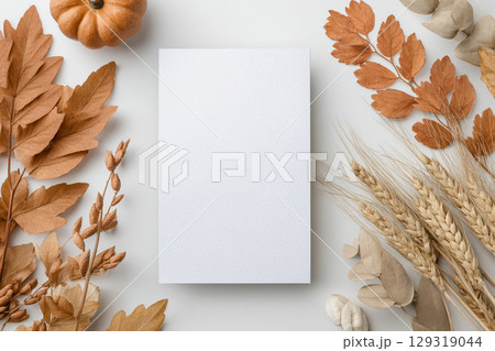 A blank card for Thanksgiving invitation mockup is centrally placed on a light surface, surrounded by various autumn decorations 129319044