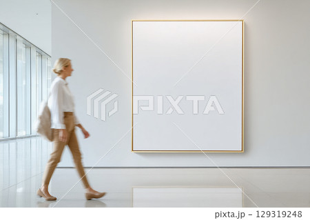 Empty large vertical frame for mockups in a modern art gallery. Blurred figure of a woman in motion walks past. 129319248