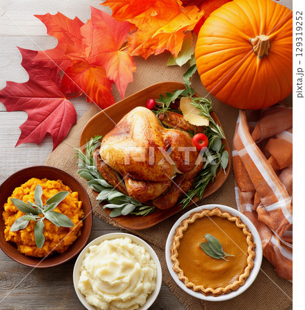 Delicious Thanksgiving feast with roast turkey, sides, and pumpkin pie surrounded by autumn decorations on a wooden table 129319252