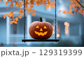 Pumpkin lantern hanging on swing decorated with autumn leaves in cozy neighborhood during Halloween celebration 129319399