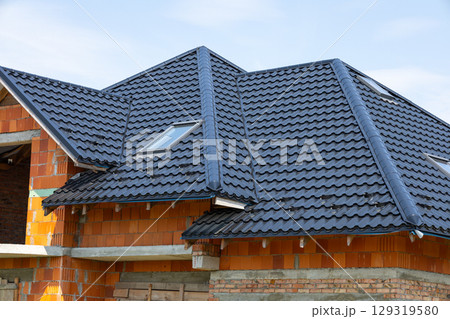 A view of a newly built house with a sleek, dark roof and skylights under a clear blue sky, indicating progress in construction 129319580