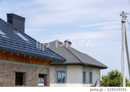 Two houses in various stages of completion are situated in a peaceful suburban area, featuring a blue sky overhead and power lines nearby Two houses in various stages of completion are situated in a peaceful suburban area, featuring a blue sky overhead and power lines nearby 129319581