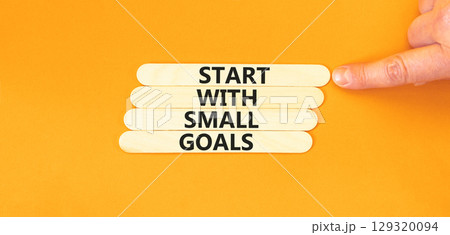 Start with small goals symbol. Concept words phrase Start with small goals on beautiful stick. Businessman's hand. Beautiful orange background. Business Start with small goals concept. Copy space. 129320094