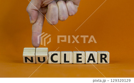 Nuclear or clear symbol. Businessman turns a cube and changes the word 'nuclear' to 'clear'. Beautiful orange background. Nuclear or clear and business concept. Copy space. Nuclear or clear symbol. Businessman turns a cube and changes the word 'nuclear' to 'clear'. Beautiful orange background. Nuclear or clear and business concept. Copy space. 129320129