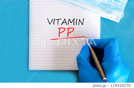 Vitamin PP symbol. Concept words Vitamin PP on beautiful white note. Doctor's hand in blue medical glove. Medical mask. Beautiful blue background. Medical healthy lifestyle Vitamin PP concept. 129320270