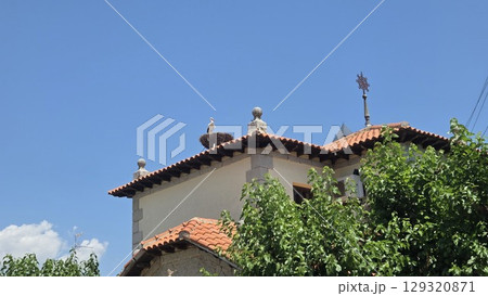 Historic spanish church with stork nest on rooftop under clear blue sky. Iglesia San Miguel Arcangel de Pedrezuela. Storks on the roof of Church of Saint Michael the Archangel in Pedrezuela, Spain 129320871