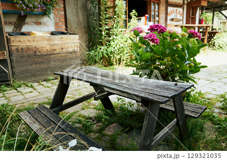 Wooden picnic table sits in a grassy area with a few potted plants nearby Wooden picnic table sits in a grassy area with a few potted plants nearby 129321035