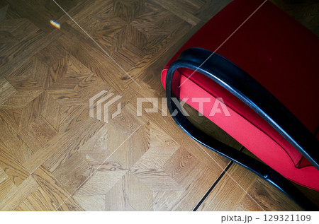 Red chair with a black handle sits on a wooden floor 129321109