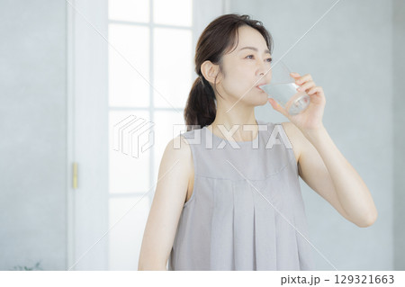 キッチンで水を飲むミドルの女性  129321663