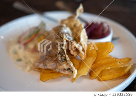 A close-up of crispy fried fish skin and potato chips, served with creamy salad and pickled red onions on plate A close-up of crispy fried fish skin and potato chips, served with creamy salad and pickled red onions on plate 129322559