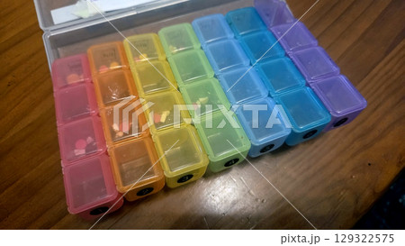 Weekly pill organizer with color-coded compartments on wooden surface 129322575