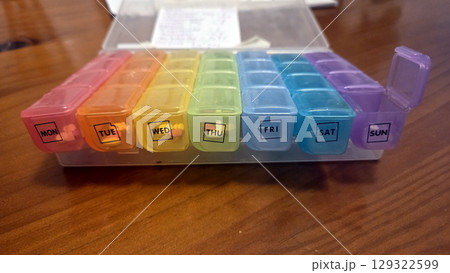Weekly pill box organizer on wooden table for daily medication management 129322599