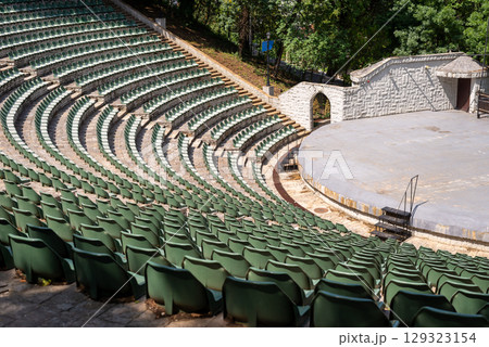 Amphitheater with concentric rows of tiered seating curving around a central stage area under an open sky 129323154