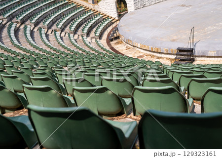 Amphitheater with concentric rows of tiered seating curving around a central stage area under an open sky 129323161